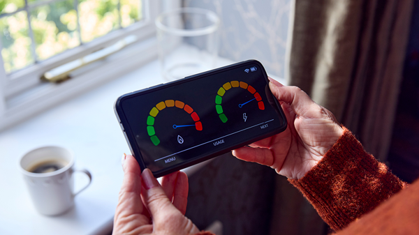 A pair of hands holding a smart meter, while a cup of tea sits on the windowsill in front.