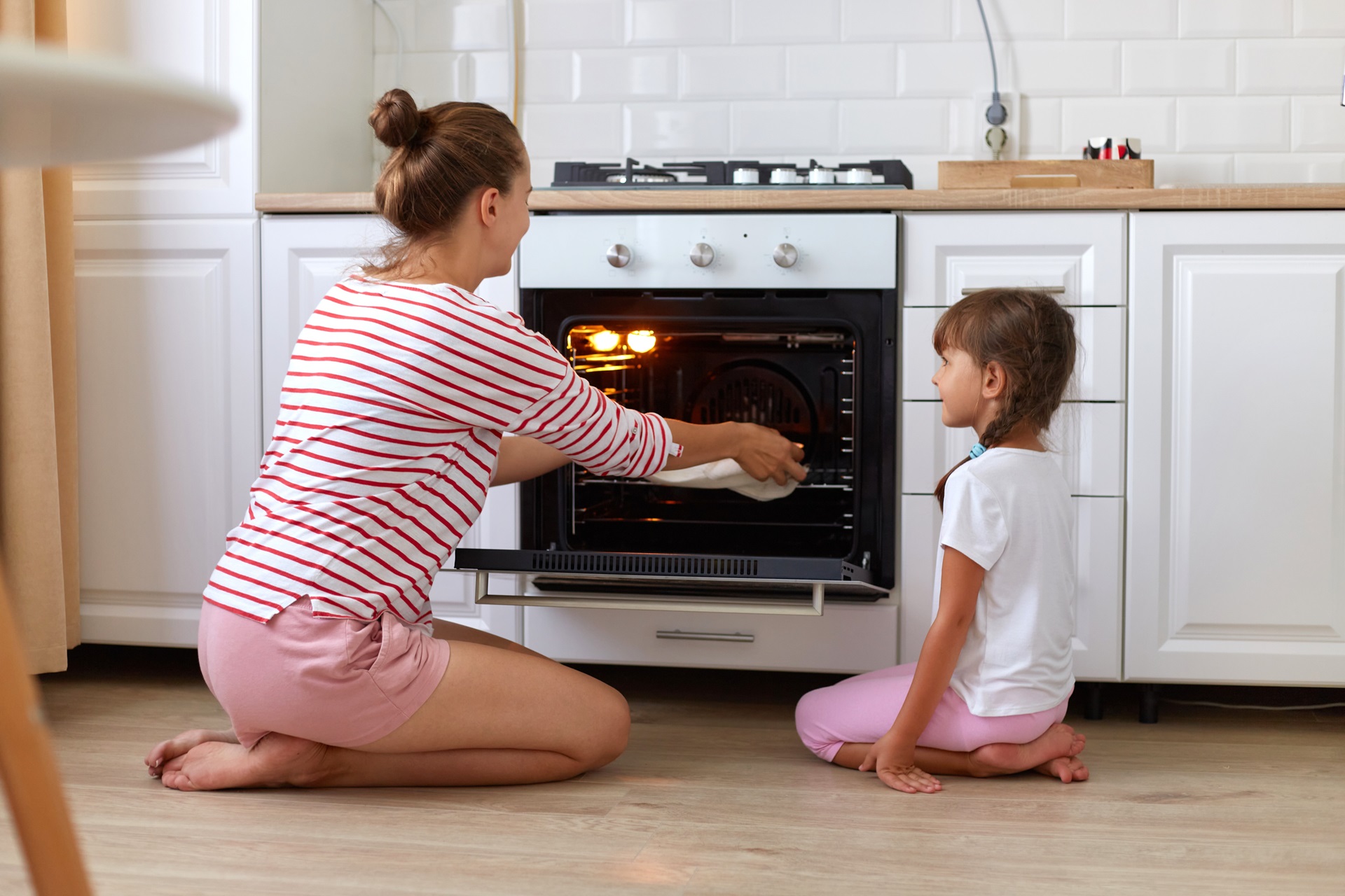 Mother and daughter kneeling on the floor putting food in an oven