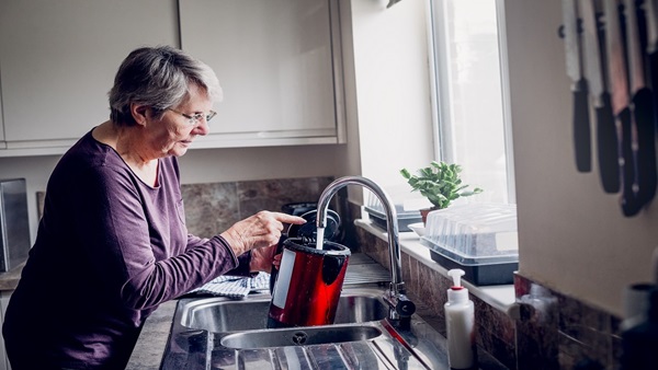 A woman standing at the sink filling up a kettle.