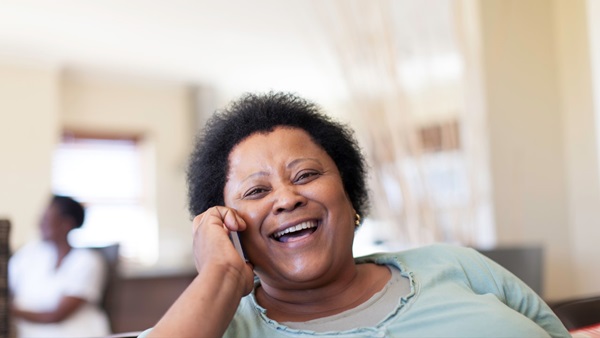 A mature woman is sat laughing as she talks on her phone.