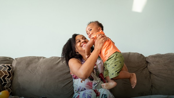 A young mother and son are sat on the sofa, laughing and playing together.