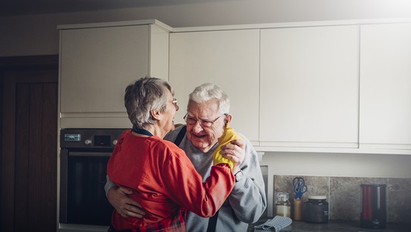 A senior couple laugh together as they dance around their kitchen.