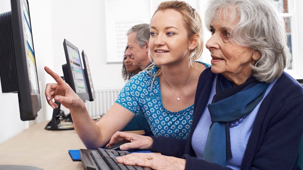 A woman assists an older lady with something on the computer