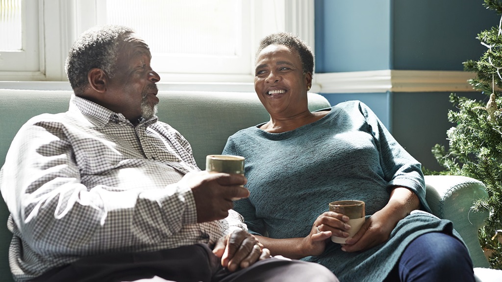 Middle-aged man and woman, sat on a sofa, chat and smile together