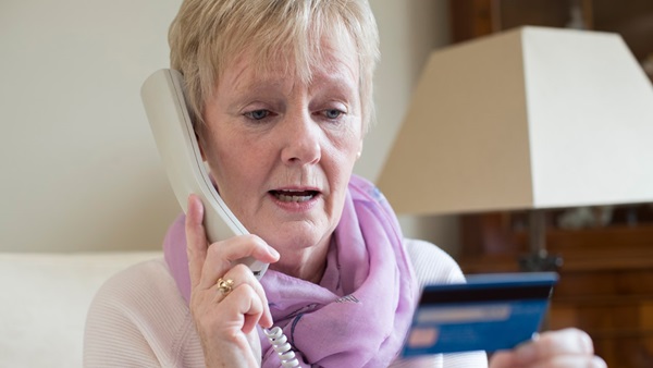 Older woman on landline phone holding a credit card ready to make a payment