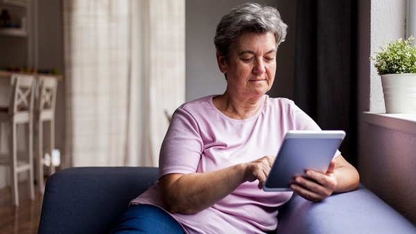 Older lady sat on sofa using an iPad tablet
