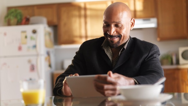 Man sits at kitchen table smiling at his iPad tablet