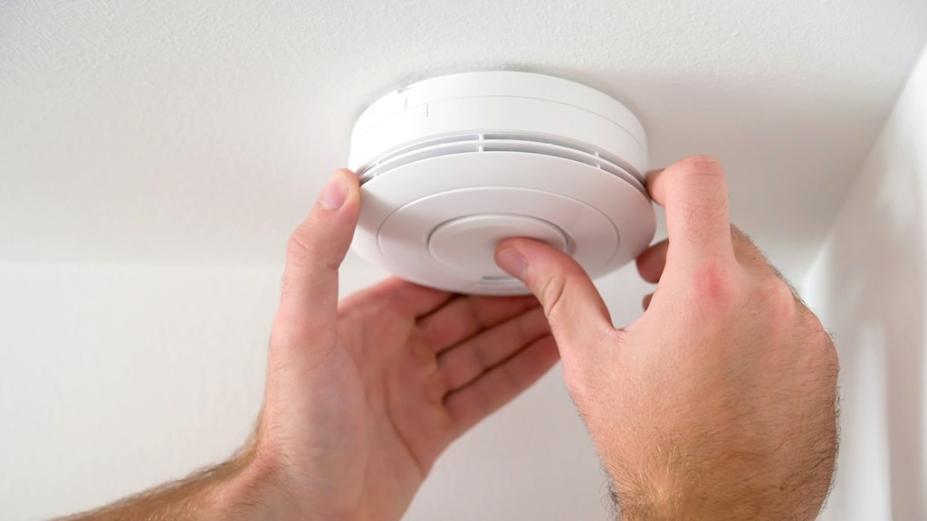 Closeup of hands testing a smoke or CO2 alarm on a ceiling for safety
